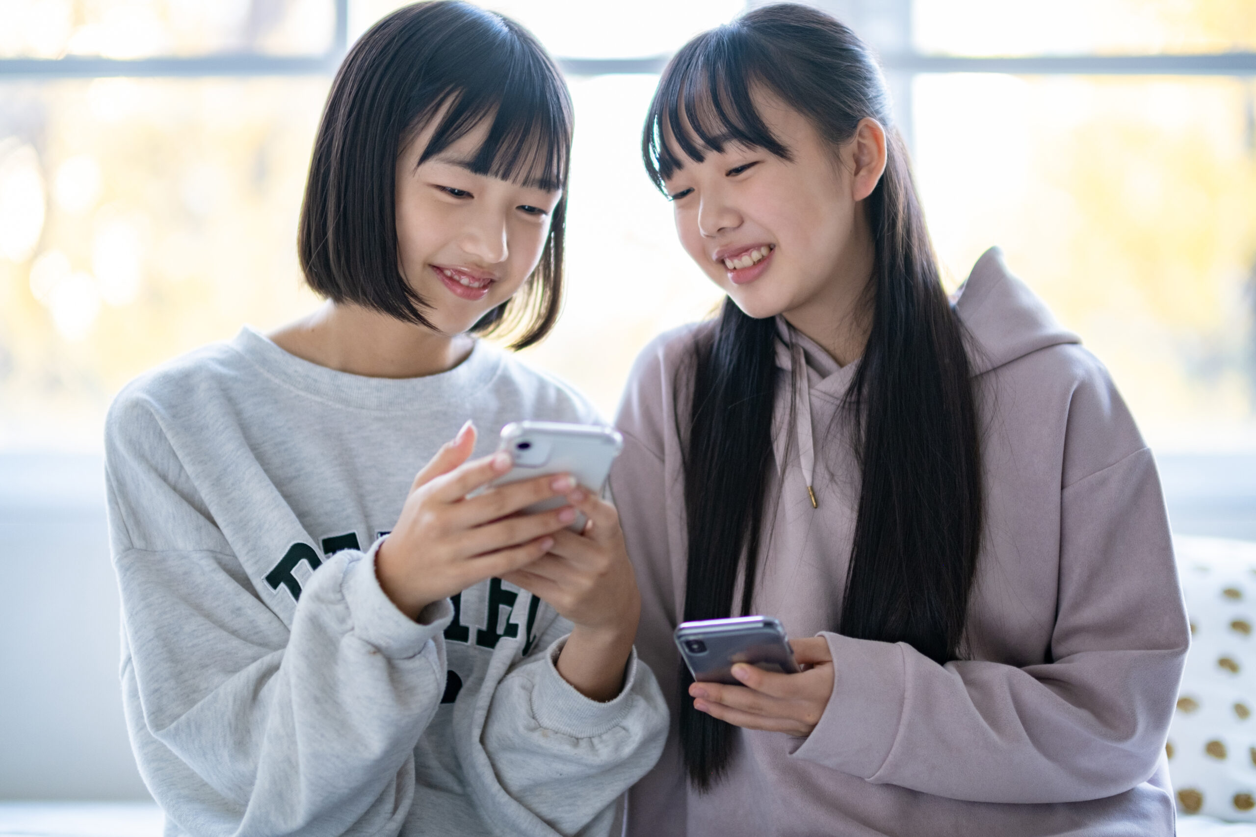 Two young girls standing close together, looking at a smartphone and smiling.