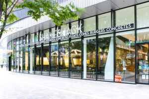 Shake Shack storefront with glass walls, a bold white sign, and green trees in front.