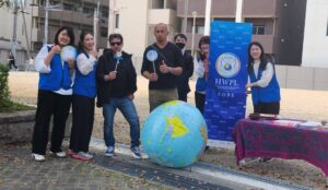 Group of volunteers posing outdoors with a large globe and a HWPL Kobe banner, smiling at the camera.