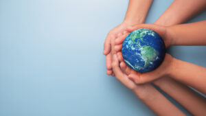 Hands cradle a small globe of Earth against a light blue background, symbolizing care for the planet.