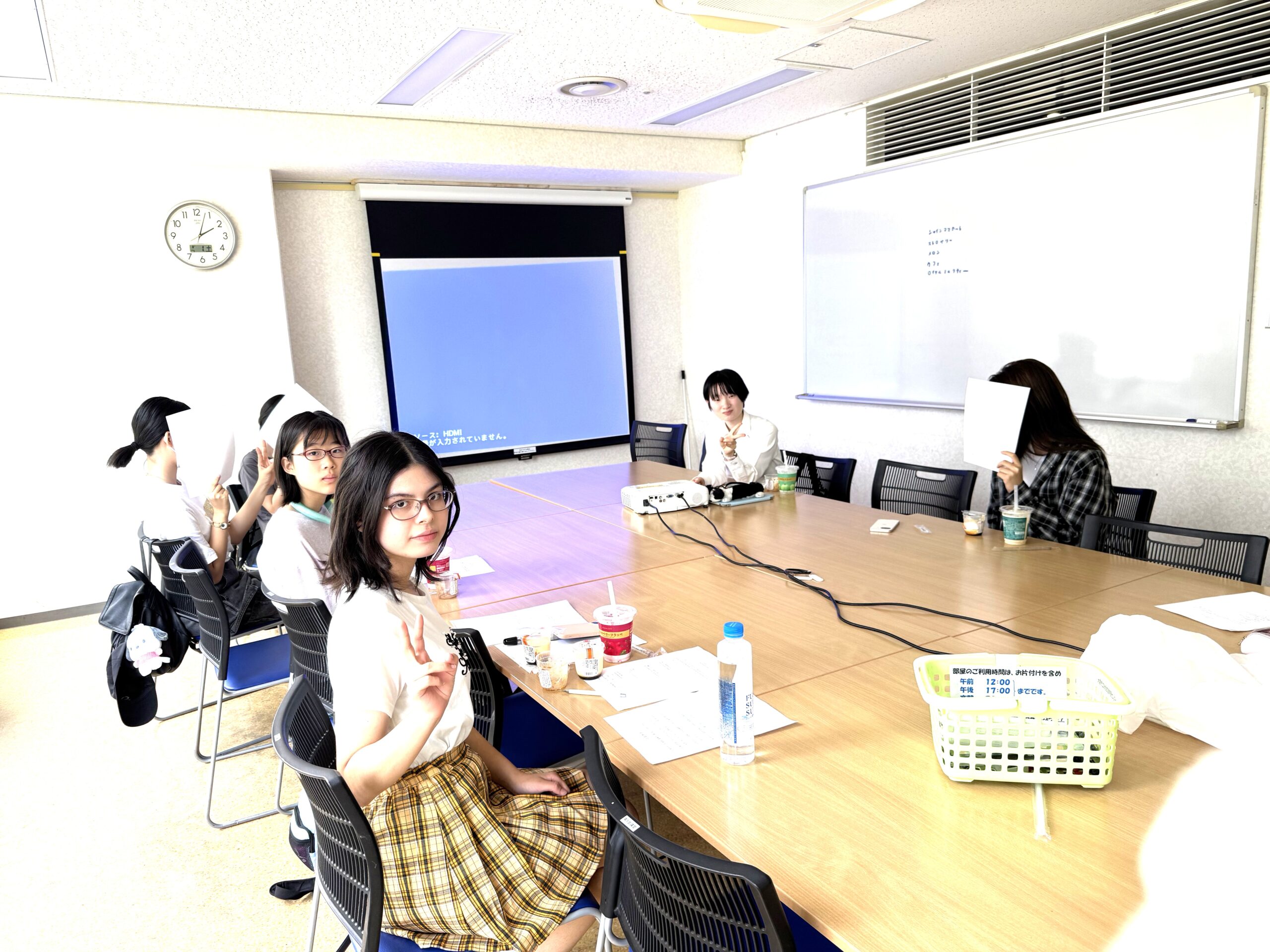 Group of students seated around a conference table in a classroom, with papers and drinks on the table and a projector screen at the front.